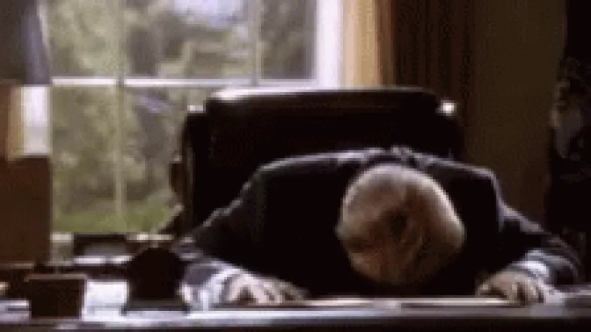 Movie scene: a man slumps face-first onto his desk.